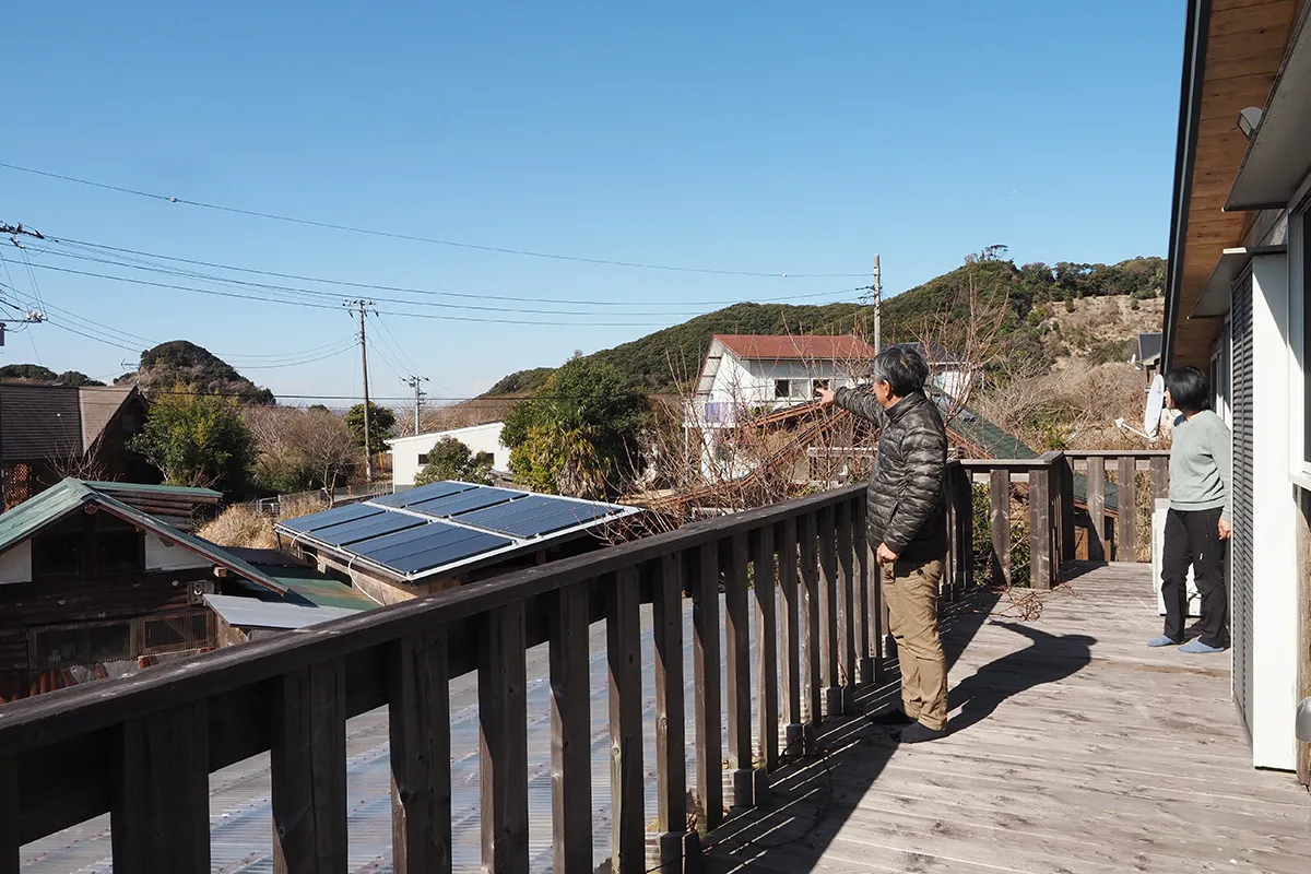 【富士山が見える方向を指さす西野さん。階下に見えるのは西野さんが建てた小屋や納屋】