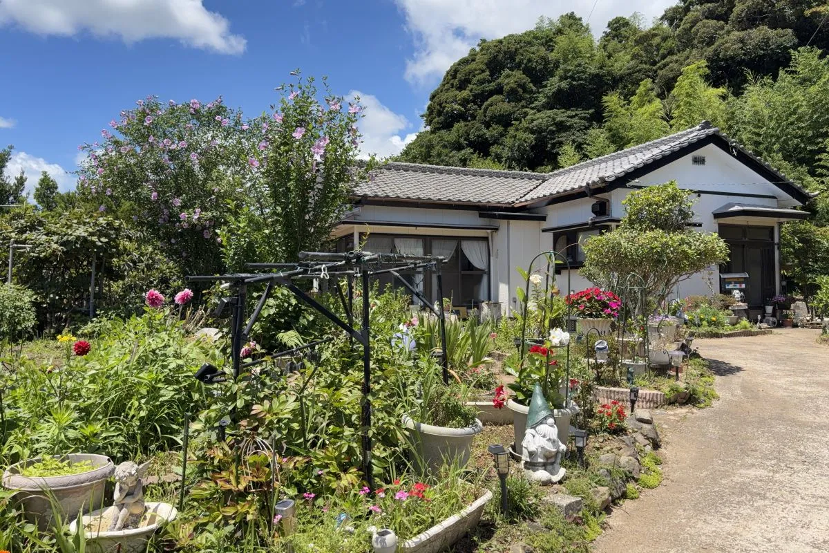 【花や緑に囲まれた佐々木さんご夫妻の住まい。里山の緑を背に、季節の花々が庭を彩ります】